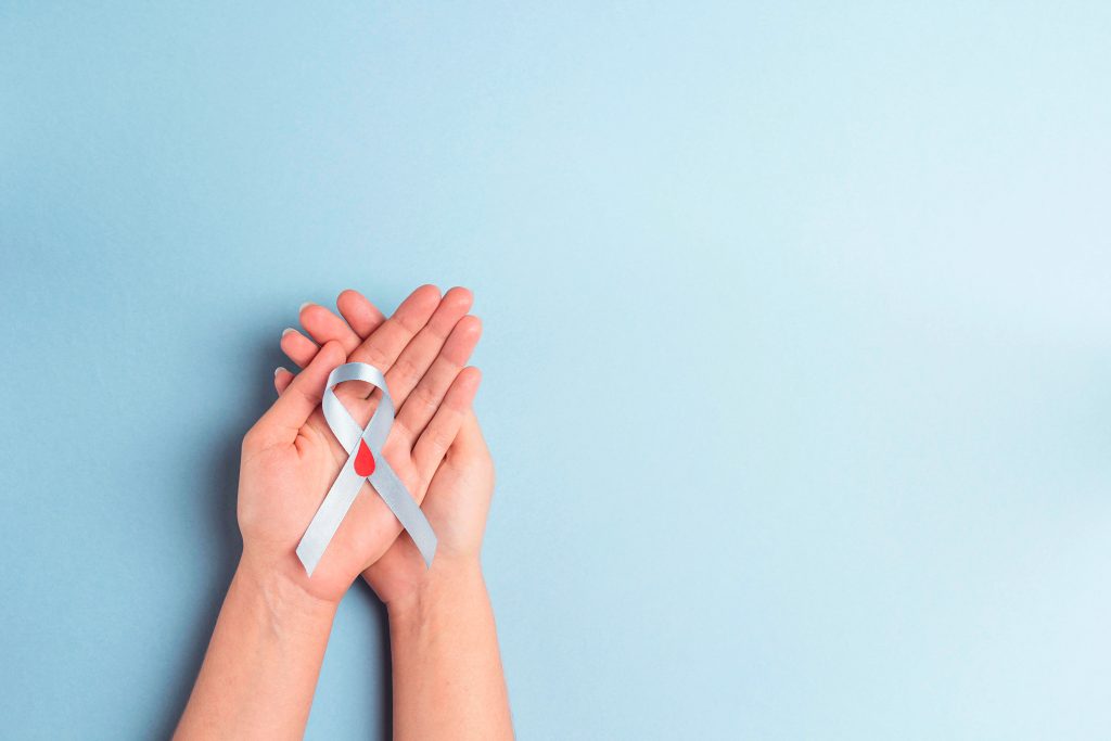 Diabetes awareness ribbon with red drop symbol in open hands